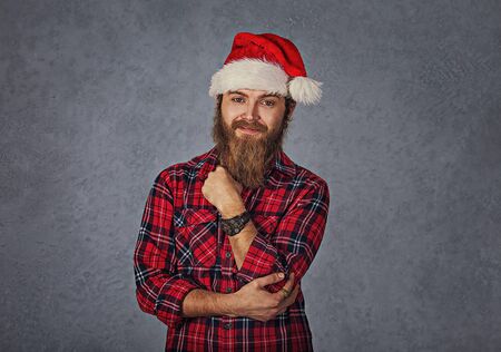 Young handsome smiling excited man in red santa hat isolated on gray grey background. Positive emotion and symbolsの写真素材