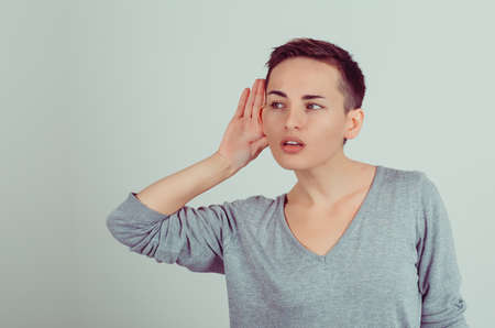 Woman holds her hand near ear and listens carefully isolated on green gray wall background. Human emotion, facial expressionの写真素材