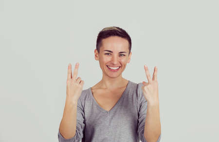 Portrait lovely happy woman showing victory or peace sign gesture isolated on light gray wall...