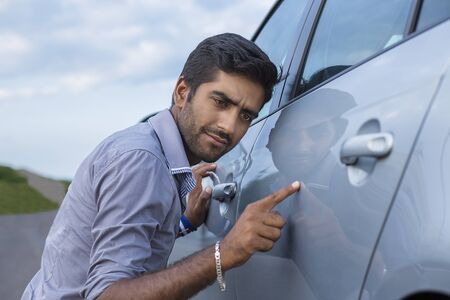 Young worried funny looking man obsessing about cleanliness of his new car. Car care and protection...