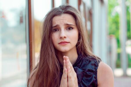 Begging. Please. Closeup portrait sad young woman praying her mom husband to buy her a dress, standing outdoors near a store window background with copy space. Human emotion facial expressionの写真素材