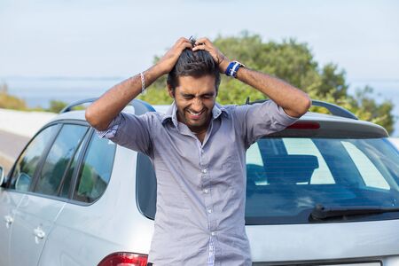 Upset driver after car accident crying hands on head, or he forgot the key while standing outdoors near his car, green tree blue sea and sky on backgroundの写真素材