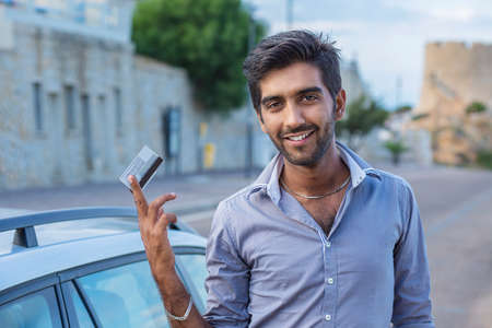 Happy smiling man standing near his new car showing credit card outdoors city road on background....