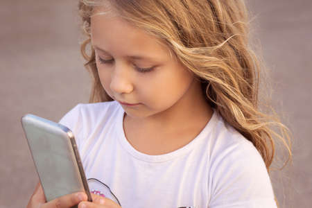 Content girl with long hair using smartphone with concentration standing outside