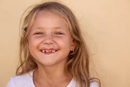 Charming happy girl with long fair hair having messy chocolate mouth and laughing at camera