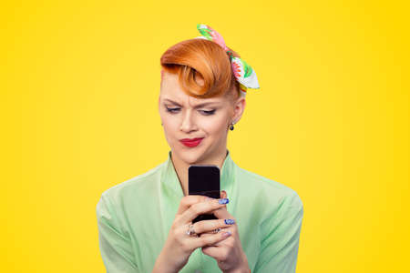 Portrait upset skeptical unhappy serious woman looking at texting on phone displeased with conversation isolated yellow background retro vintage 50's style. Negative human emotion face expressionの写真素材