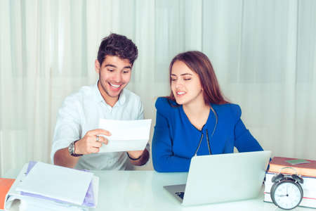 Excited bright man having great news in letter while sitting in office with female colleague near....