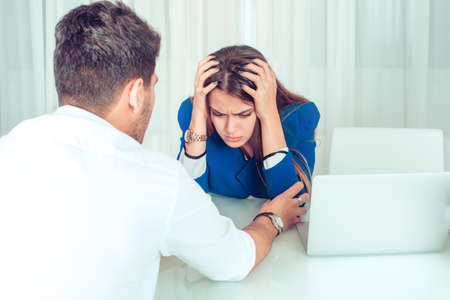 Anonymous man consoling young woman in stress and worries while sitting at table in office. Boss...