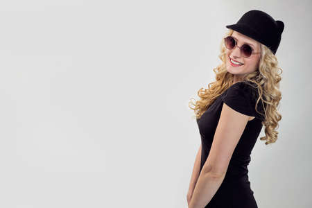 Side view of trendy blond woman in black t-shirt and cap wearing sunglasses and posing flirty