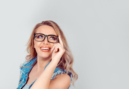 Thinking and wondering adult pretty blonde woman touching glasses and looking away on gray background.の写真素材