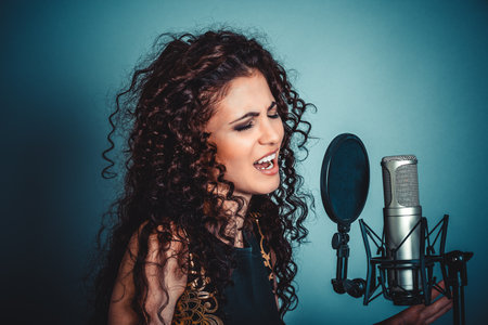 Singer. Closeup portrait head shot sexy beautiful happy young woman lady girl singing karaoke with microphone isolated blue background wall. Positive human emotion expression feeling life perceptionの写真素材
