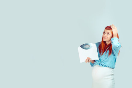 Young scared pregnant woman having overweight and holding weight scales looking up in worries isolated on blue. I got some extra kilos during pregnancy conceptの写真素材