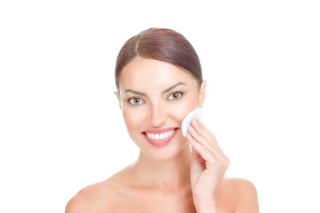 Beauty, skin care and people concept - closeup portrait young woman applying lotion to cotton disc pad, washing her face smiling isolated on white background. Mixed race latina caucasian modelの写真素材