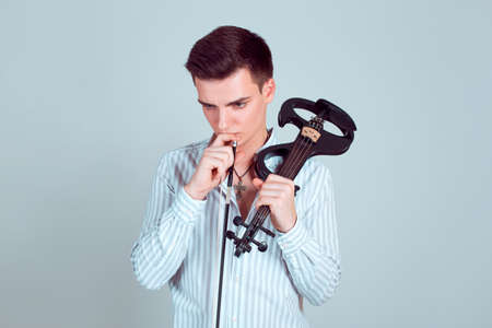 Young handsome man holding violin with fiddle and looking pensive in contemplation on blue backgroundの写真素材