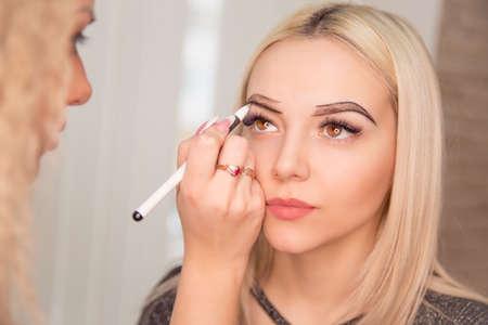Microblading, micropigmentation eyebrows work flow in a beauty salon. Woman having her eye brows drawn and tinted with black pencil, preparing for semi-permanent makeup for eyebrows. Focus on eyebrowの写真素材