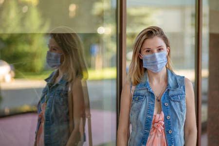 Beautiful businesswoman, young woman, in medical protective mask on her face, in formal jacket standing outdoors, looking at camera. Coronavirus, virus, epidemic, pandemic covid-19 conceptの写真素材