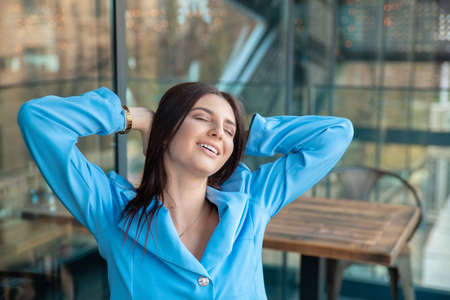 Happy and relaxed. Happy young business woman eyes closed hands raised behind head relaxing. Stress relief techniques. Girl sitting outdoors at office or home balcony in formal wear with long hairの写真素材