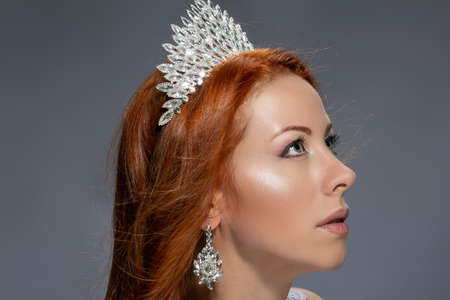 Beauty queen. Woman in profile with diamond crown on head looking up to side posing isolated on grey background. Multicultural Caucasian Irish modelの写真素材