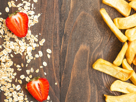 Healthy vs unhealthy food and dieting concept. Oat flakes and fresh strawberries vs french fried potatoes isolated on woody table studio background with copy space. Flat lay, view from top.の写真素材