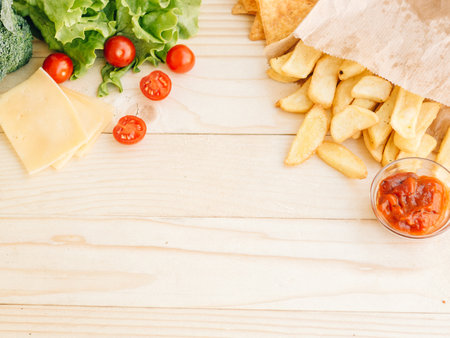 Healthy vs unhealthy food, dieting concept. Lettuce salad, cherry tomatoes on left side and french fried potatoes on the right on woody table studio background with copy space. Flat lay, top viewの写真素材