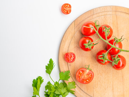 Healthy food and dieting concept. Red cherry tomatoes and persil stem, stalk and leaves on woody cutting board isolated on white color studio background with copy space. Flat lay, view from top.の写真素材