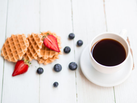 Healthy delicious breakfast early in the morning. Fresh Waffles, blueberries, strawberries, hot coffee isolated on the old white wooden background.の写真素材
