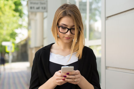 Pensive attractive trendy woman female girl outside near mall store office texting, sending a message, browsing in internet and social media profile, using application on smartphone for calling taxiの写真素材