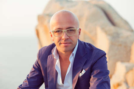 Portrait of a confident pensive Caucasian bald man in eyeglasses looking at you camera sitting...