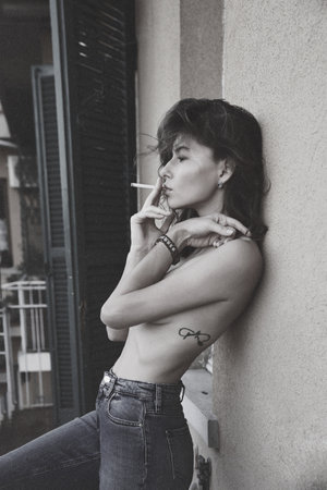 Fashion style portrait of a beautiful woman smoking a cigarette and posing in lingery on an Italian balcony and looking ahead thoughtful, pensive thinkingの写真素材