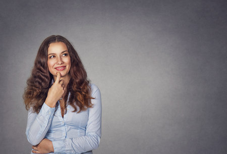 Portrait of an attractive young brunette thoughtful woman smiling looking up isolated on gray grunge wall backgroundの写真素材