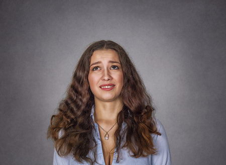 closeup portrait headshot cute unhappy woman looking up isolated on gray wall background with copy space above head. Human face expressions, emotions. funny confused skeptical girl femaleの写真素材