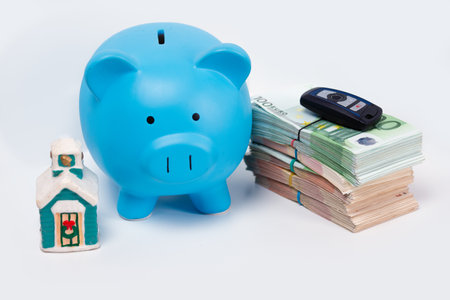 Stack pile of european money, Euro cash currency with a car key on it, a piggy bank next to it and a home on it isolated on white background. Savings for a new home and car, real estate property mortgage leasing concept.の写真素材
