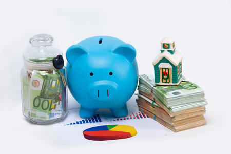 Stack pile of european money, Euro cash currency, piggy bank with key on it and a home on graphic chart isolated on white background. Savings for a new home, real estate property mortgage concept.の写真素材