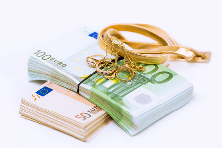 Gold and money. Stack pile of European union currency bills, euro banknotes and a bunch of golden jewelry isolated on white background. Savings bank account concept. Finances, liquidity.の写真素材