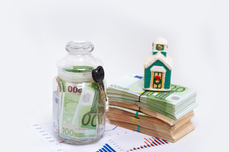 Stack pile of european money, Euro cash currency in a jar with a key on a graphic chart and a home on it isolated on white background. Savings for a new home, real estate property mortgage business conceptual image.の写真素材