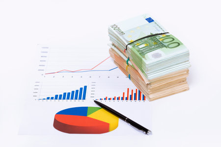 Stack pile of european money, Euro cash currency on a graphic chart and a pen on it isolated on white background. Savings for a investing in stock market business conceptual image.の写真素材