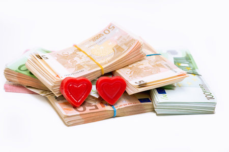 Stack pile of european money, Euro cash currency and two hearts on it isolated on white background. Savings for a a marriage, a new family conceptual image.の写真素材