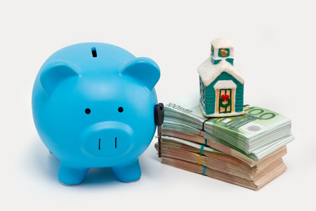 Stack pile of european money, Euro cash currency, a piggy bank with a key on it and a home on it isolated on white background. Savings for a new home, real estate property mortgage concept.の写真素材