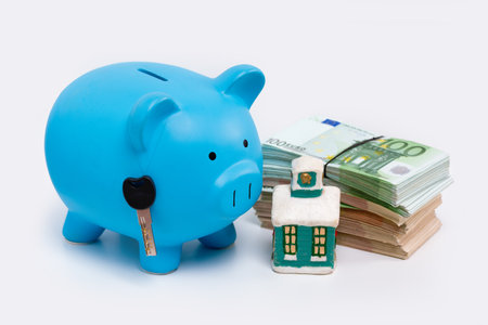 Stack pile of european money, Euro cash currency, a piggy bank with a key on it and a home on it isolated on white background. Savings for a new home, real estate property mortgage concept.の写真素材