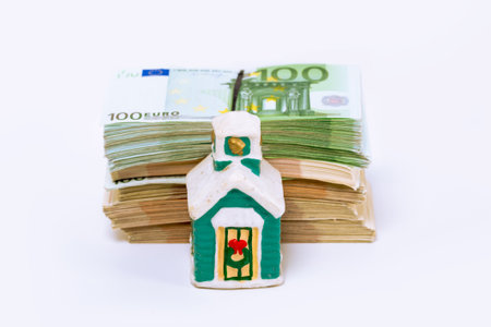 Stack pile of european money, Euro cash currency and a home on it isolated on white background. Savings for a new home, real estate property mortgage conceptual image.の写真素材
