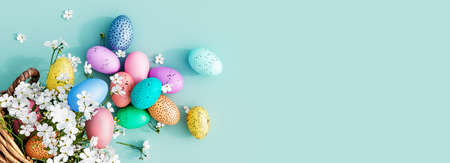 Bunch of colorful eggs in a basket with spring flowers on blueの写真素材