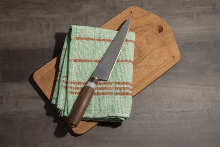 Big kitchen knife with wood and ivory handle lying on an old cutting board and kitchen ragの写真素材