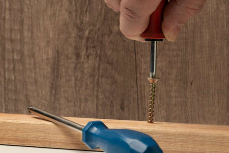 Gloved hand of worker tightens screw nut with adjustable metal wrench or french wrench in wooden...