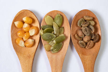Different seeds -corn, squash, coffee- in wooden spoons on a white surface