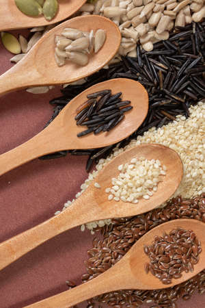 Different seeds -quinoa, pumpkin, rice, sunflower- in wooden spoons on a surface of different seeds and brown backgroundの写真素材