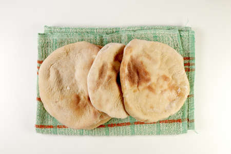 freshly baked pita or arabic breads on a rustic cloth and a wooden board on a white surface
