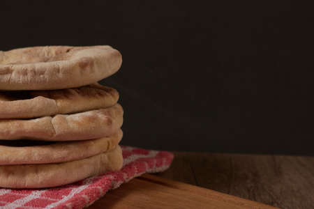 several pita breads stacked on a rustic cloth and a cutting board on a wooden table with black backgroundの写真素材