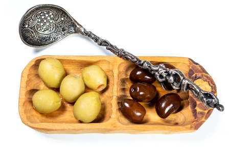 Black and green olives in a small wooden bowl, a spoon for olives on a white surface background Top Viewの写真素材