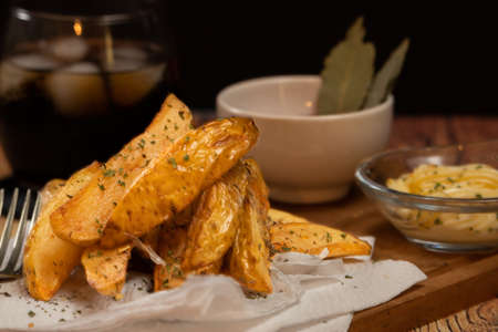 Rustic or country style fries with herbs in a ceramic bowl on a wooden board with barbecue sauce and...