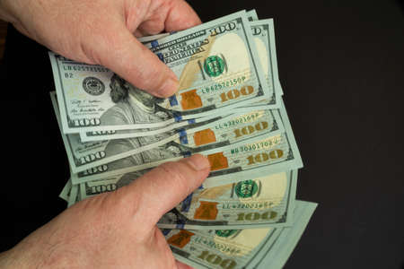 Hands counting American 100 dollar bills on a black background